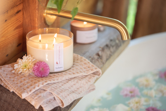 Elegant soy wax candle in a glass jar. Placed by a bath tub, with matt gold tap and flowers. Hand poured by The Eden Collections. 