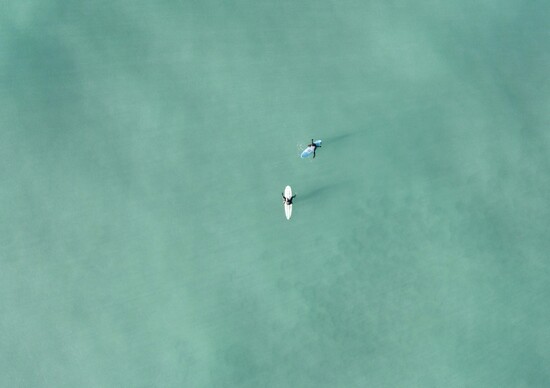 two surfers sitting on boards floating on a blue ocean