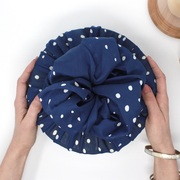 Circular cake tin wrapped in a navy spotty fabric gift wrap, held in 2 hands. 