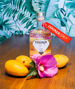tourer gin - mango gin shot with hibiscus flower and three mangos laying in front of bottle.