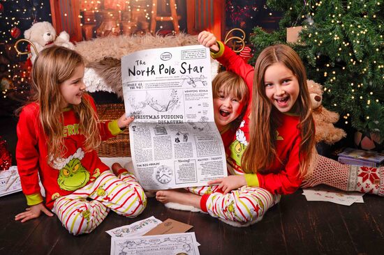Three smiling children are wearing christmas pyjamas and holding a copy of the North Pole star newspaper