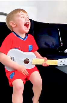 Young child singing and playing guitar while listening to personalised music with his name and birthday in the lyrics, created by My First Music