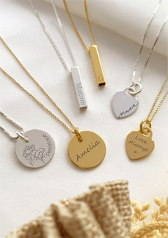 A range of personalised silver and gold necklace displayed with a gift bag & dried flowers